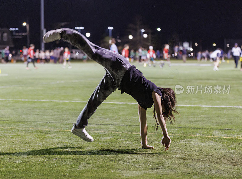 Сheerleader practicing exercises at the soccer field in the evening.